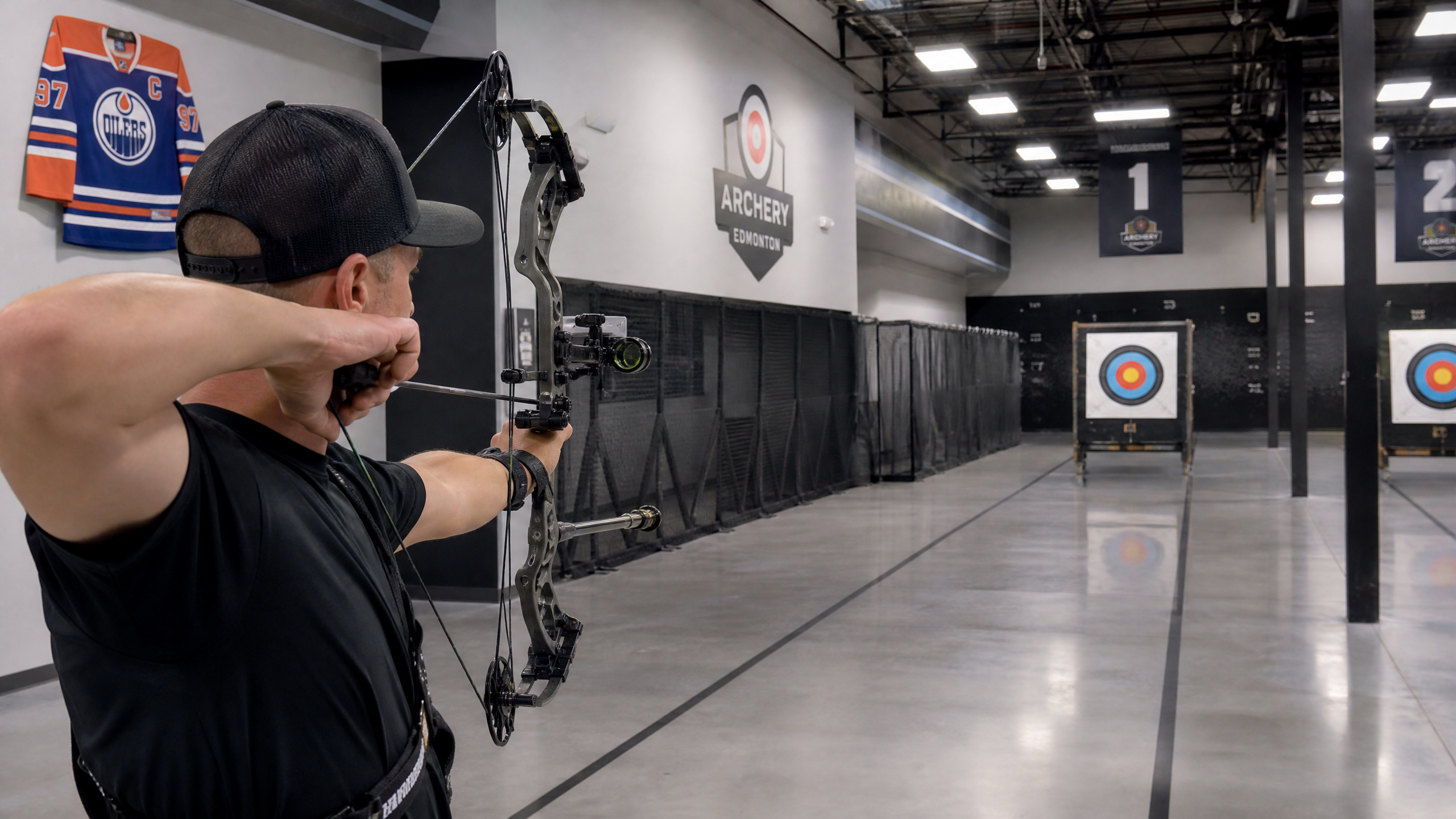 Modern indoor archery range with a compound bow and an Edmonton Oilers jersey on the wall