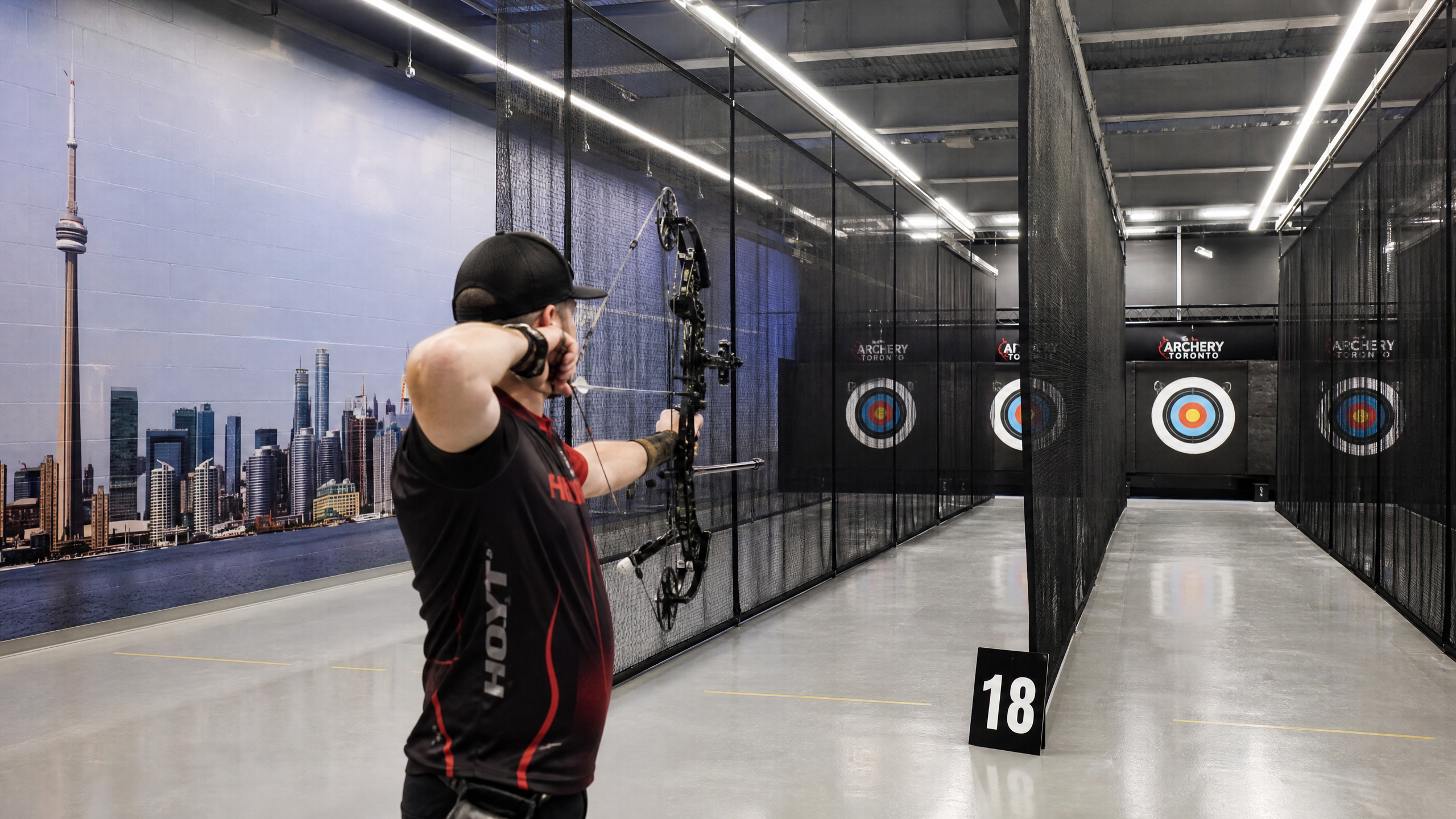 Modern indoor archery range with a compound bow and a city skyline mural
